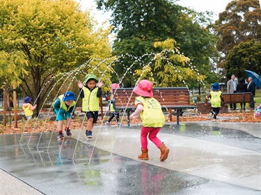Children running under water fountains at Ballam Park play space